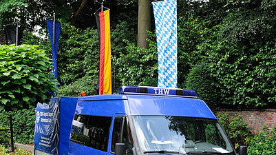 Ein Auto des THW steht vor den Fahnen von Bayern, Deutschland und Europa