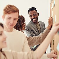 Mehrere Kolleginnen und Kollegen stehen an Pinnw&auml;nden und zeigen auf Post-Its