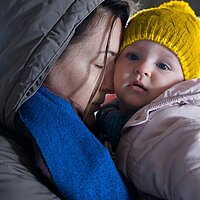 Eine Mutter h&auml;lt ihr Kind im Arm und schlie&szlig;t die Augen. Beide tragen warme Kleidung. 