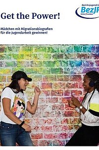 Titelseite der Publikation "Get the Power". Abgebildet sind zwei junge Frauen vor einer bunten Backsteinwand, die zusammen tanzen. 