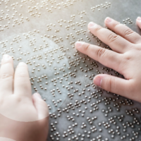 Zwei H&auml;nde ertasten einen Text in Brailleschrift.