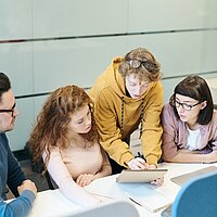 Eine junge Person zeigt den Mitarbeitenden etwas am Laptop