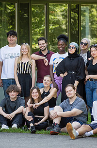 Eine gro&szlig;e und diverse Gruppe von Jugendlichen schaut f&uuml;r ein Gruppenfoto l&auml;chelnd in die Kamera.