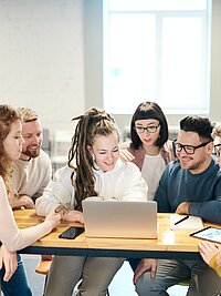 Eine Gruppe junger Menschen sitzt gemeinsam an einem Laptop und arbeitet.
