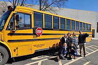 Ein paar Sch&uuml;ler und zwei Lehrer posieren vor dem gelben Schulbus.