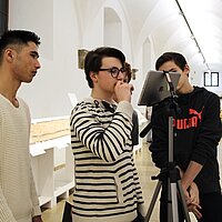 Drei junge M&auml;nner machen eine Aufnahme mit IPad in einem Museum und schauen gr&uuml;belnd auf den Monitor