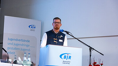 Eine Person am Mikrofon erl&auml;utert Hintergr&uuml;nde zum Schwerpunktthema Queere Jugendarbeit