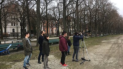 Auf dem Bild sieht man sechs Personen, die vor einer aufgebauten Kamera auf einer Wiese stehen.