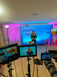 Im Studio steht die Moderatorin. Rechts auf der Leinwand h&auml;lt die ehemalige bayerische Jugendministerin Trautner eine Videobotschaft. 