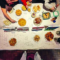 Ein Tisch mit Speisen wird von Kindern angerichtet, fotografiert von oben