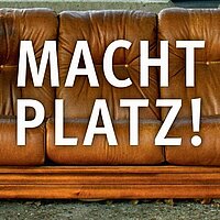 Gro&szlig;e wei&szlig;e Schrift: MACHT PLATZ! Im Hintergrund eine braune Couch.