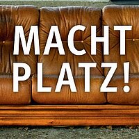 Gro&szlig;e wei&szlig;e Schrift: MACHT PLATZ! Im Hintergrund eine braune Couch.