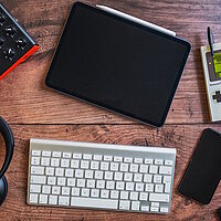 Ein Holztisch von oben. Auf dem Tisch liegen Kopfh&ouml;rer, Keyboard, Tastatur, Tablet und Handy