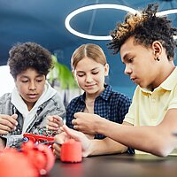 Drei Jugendliche t&uuml;fteln zusammen an einem technischen Experiment 