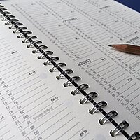 Ein offener Ringbuchkalender. Ein Stift liegt auf ihm.
