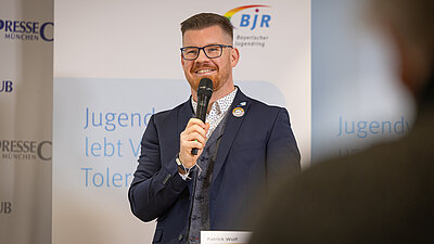 Eine Person stehend am Redepult mit Mikrofon in der Hand