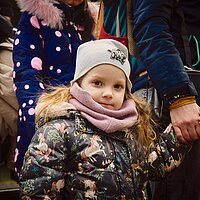 Ein M&auml;dchen in Winterkleidung geht an der Hand und schaut in die Kamera